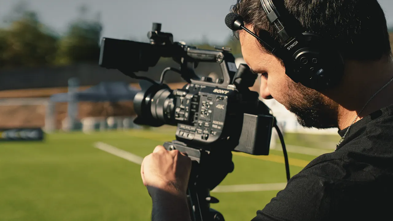 Operador de câmara com auscultadores a operar uma Sony 4K num campo de futebol